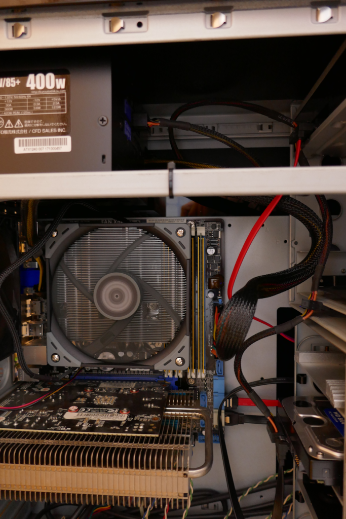 自作PCの内部の写真。 下方にファンレス ヴィデオ カードがある。 中央にファンが回転しているCPUクーラーがある。 クーラーの右横に黄金色のヒート スプレッダーが付いたメイン メモリーが2枚挿入されている。 奥にマザーボードがある。 右端にHDDが見える。 左上に電源装置の筐体がある。