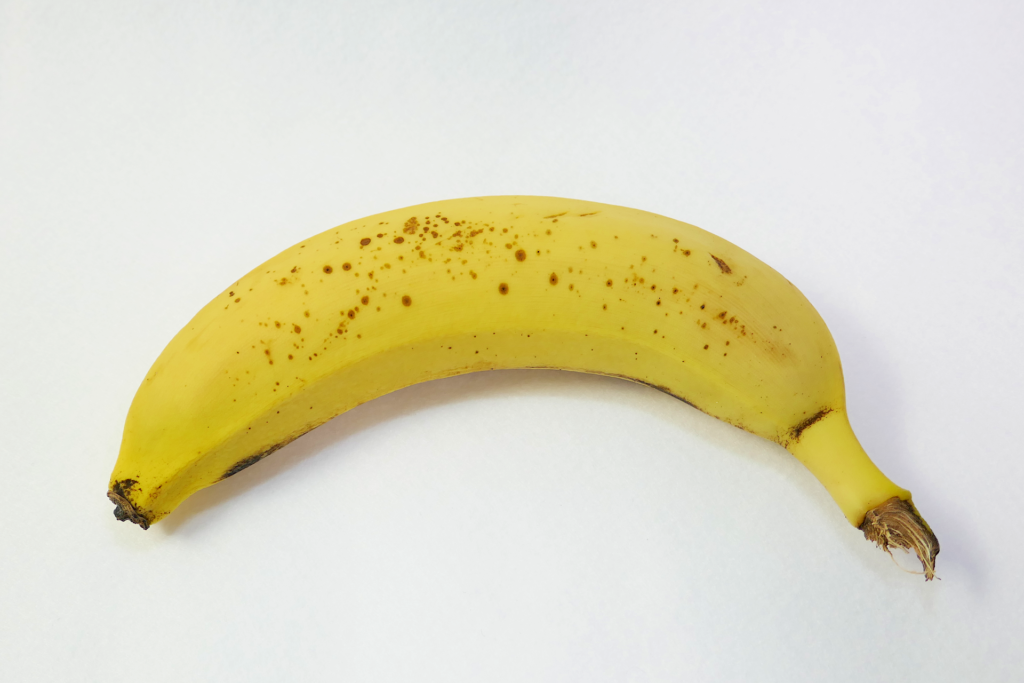 1本のバナナを撮影した写真。 白色のフェルトの上に付け根を右向きにして置かれている。