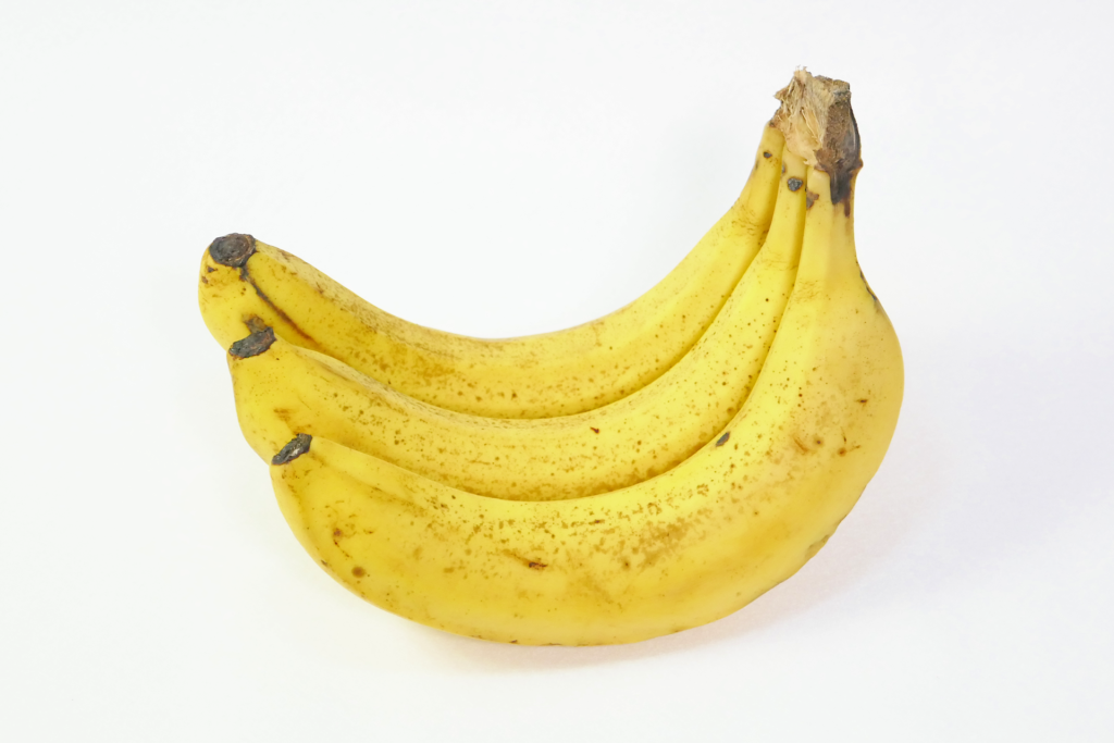 黄色いバナナの写真。 先が左を向いて3本が繋がっている。 白色のフェルトの上に置かれている。 茶色の斑点がある。
