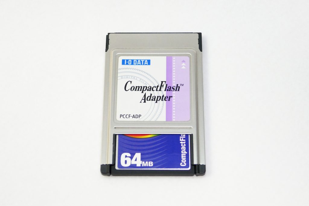 CompactFlashアダプターを撮影した写真。 PC Cardスロット差し込み用端子の側を上向きにして置かれている。 向かって下側にCompactFlashメモリー カードが装着されている。