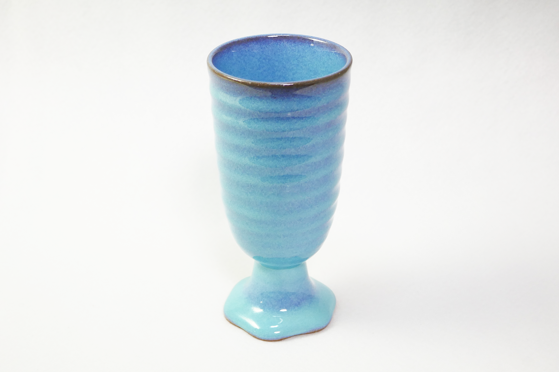 青色から水色の濃淡のある陶製のカップを撮影した写真。 台と一体化した太く短い脚に深くて長い容器が付いている。