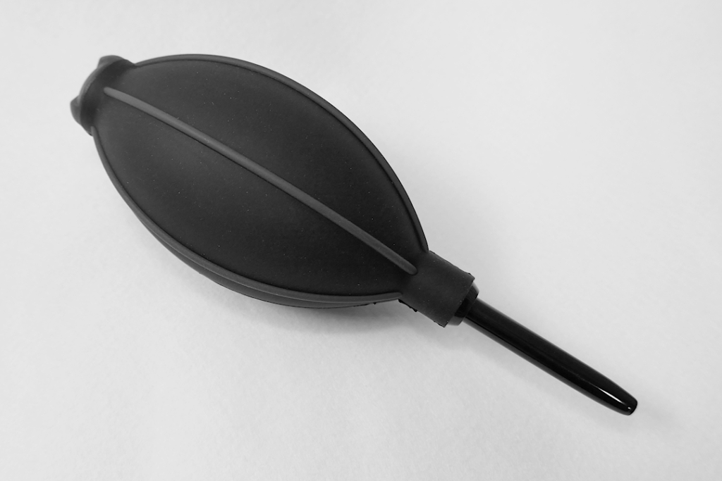 黒色のシリコーン エラストマー製のハンディ ブロワーの写真。 白色のフェルトの上にノズル先端を右下向きにして置かれている。