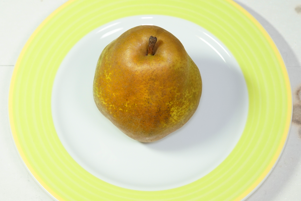 丸い皿の上に置かれている1個の洋梨を撮影した写真。