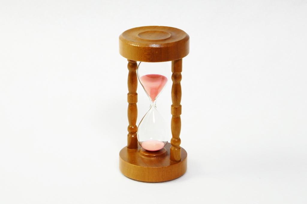木とガラスで出来た砂時計を撮影した写真。 流れ落ちている砂はピンク色をしている。