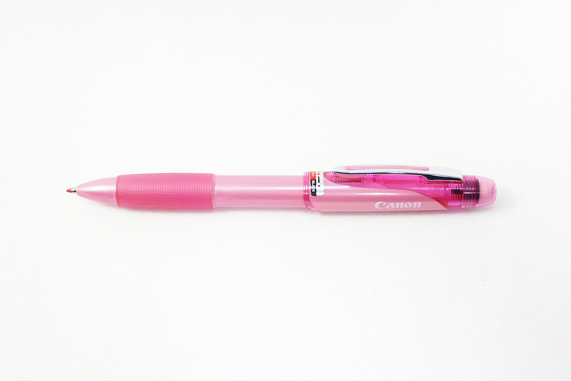 ピンク色のデザインの多機能ペンを撮影した写真。 メカニカル ペンシルと、赤色と黒色のインクのボールポイント ペンを切り替えられるようになっている。 ペン先を下向きにして置かれている。