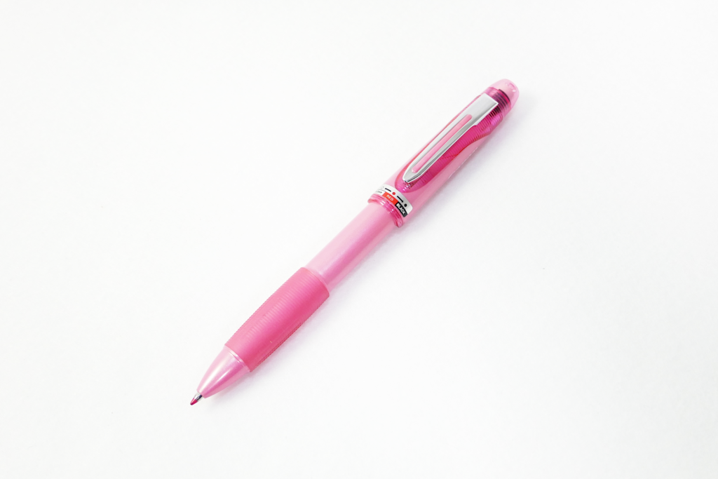 ピンク色のデザインの多機能ペンを撮影した写真。 メカニカル ペンシルと、赤色と黒色のインクのボールポイント ペンを切り替えられるようになっている。 ペン先を左下向きにして置かれている。