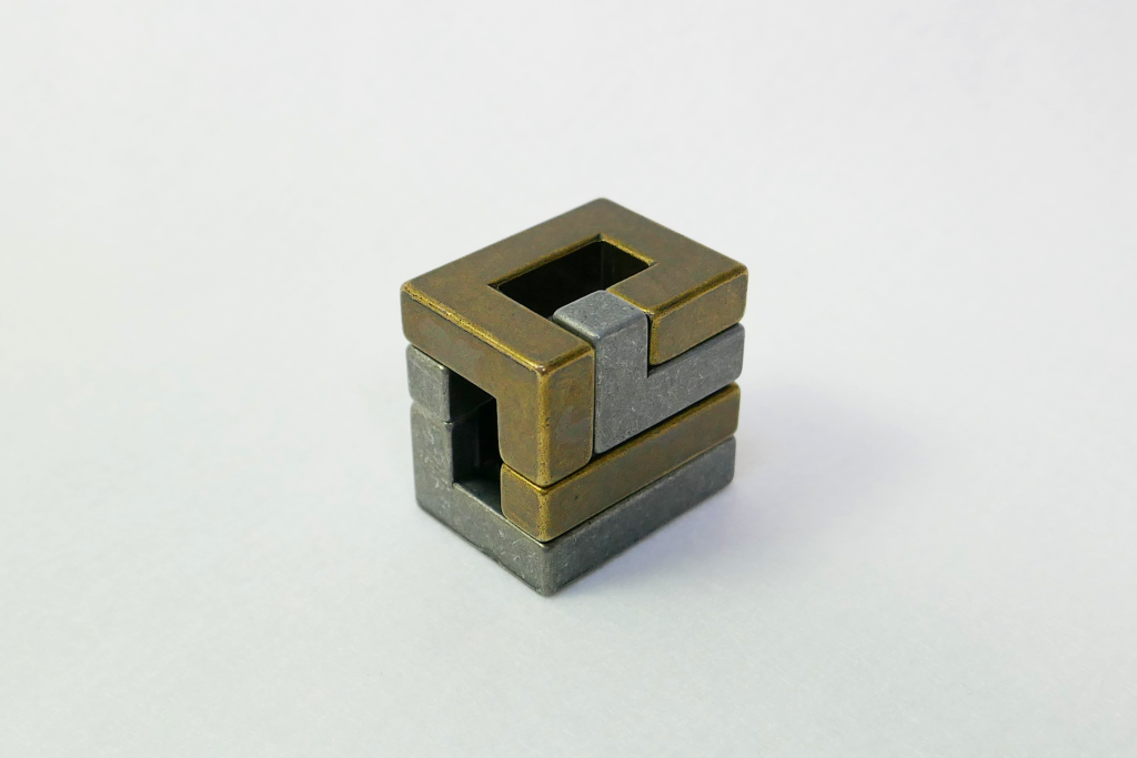 非鏡面の金属製の立体パズルであるHuzzleを撮影した写真。 直方体状に組み上がった状態。 白色のフェルトの上に置かれている。