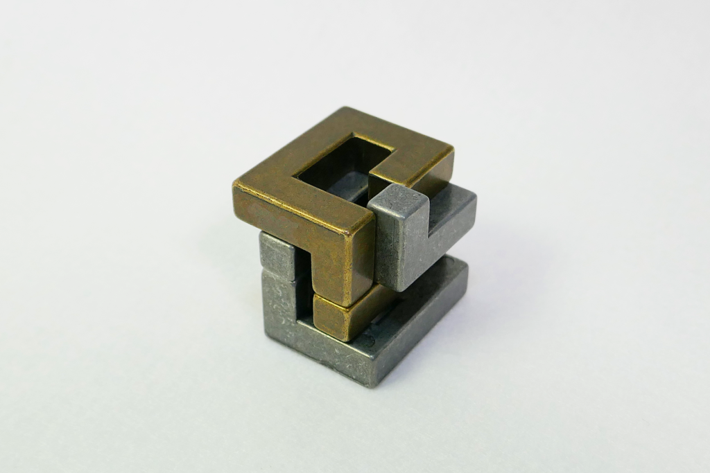 非鏡面の金属製の立体パズルであるHuzzleを撮影した写真。 ピースが少しずらしてある。 白色のフェルトの上に置かれている。