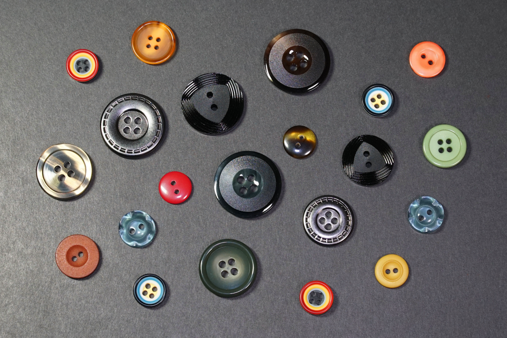 ソースルー タイプの多様なボタンを撮影した写真。 黒い紙の上に多数のボタンが置かれている。