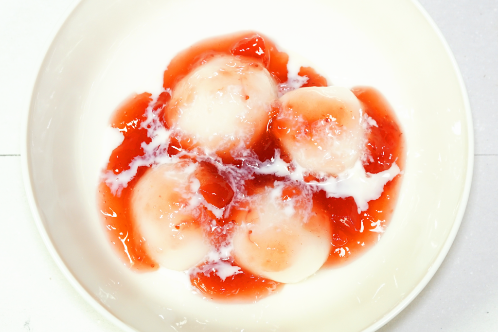 赤色のベリーのミックス ジャムと白色の練乳が掛けられている、皿に置かれた白玉を撮影した写真。