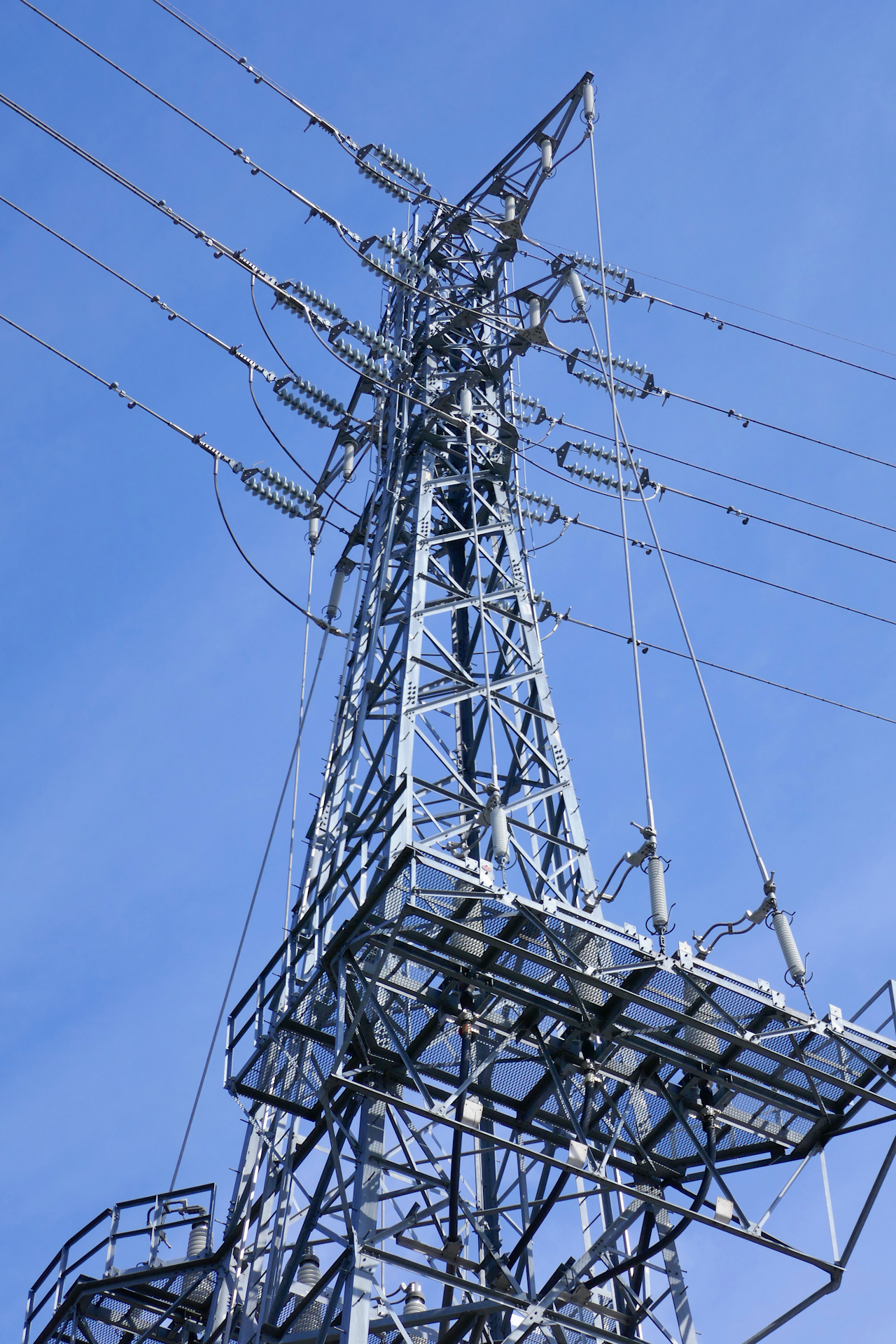 高圧送電用鉄塔を下から見上げて撮影した写真。 青空を背景に鉄塔が伸び、多数の碍子が取り付けられている。