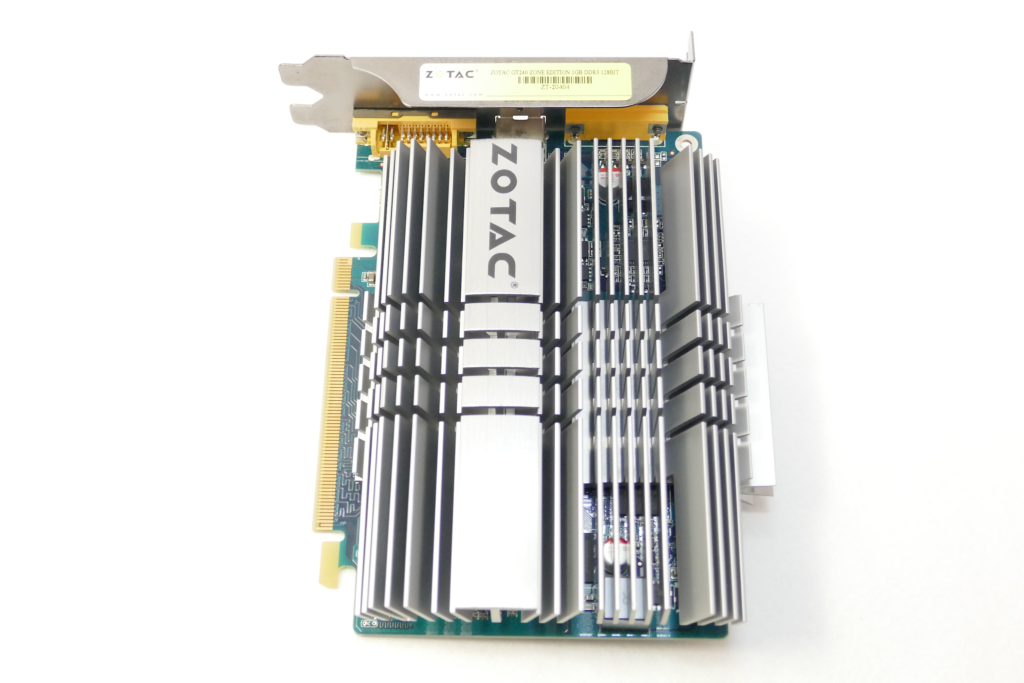 ファンレス ヴィデオ カードのZOTAC GeForce GT 240 1GB ZONE Editionを撮影した写真。 ブラケットを上向きにして置かれている。 美しいアルミニウム製の分厚いフィンの大型ヒート シンクが搭載されている。