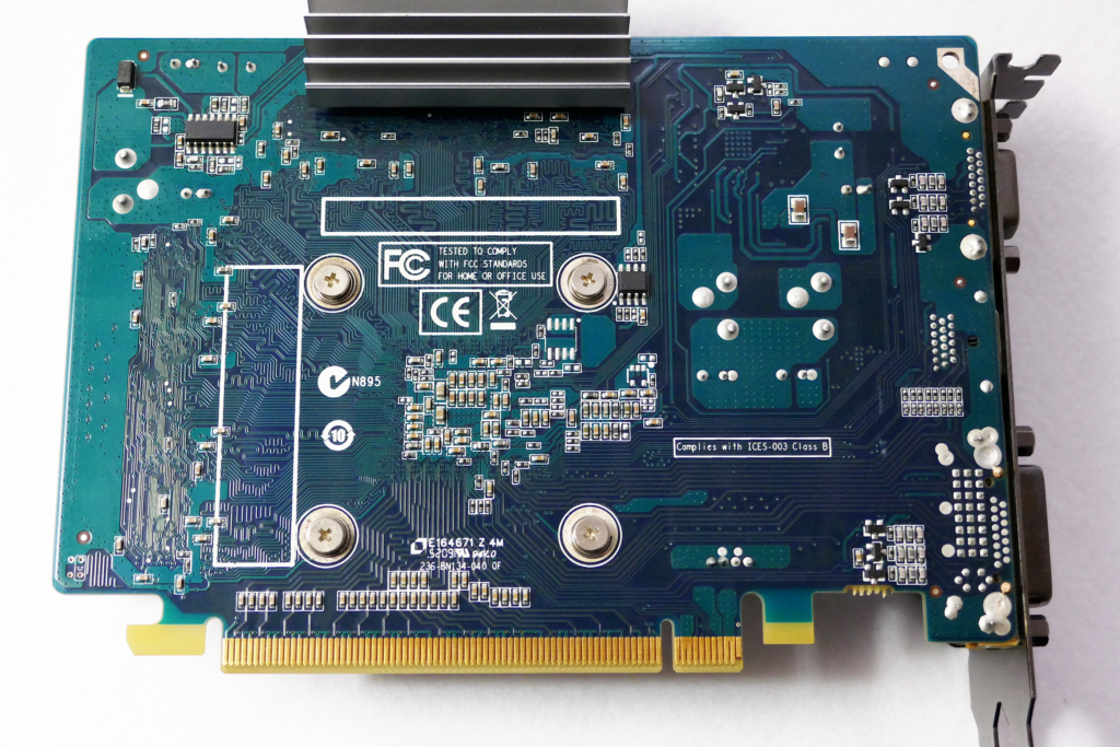 ファンレス ヴィデオ カードのZOTAC GeForce GT 240 1GB ZONE Editionの裏面を撮影した写真。 プリント回路基板上に複雑な配線パターンが見え、多くの素子が実装されている。