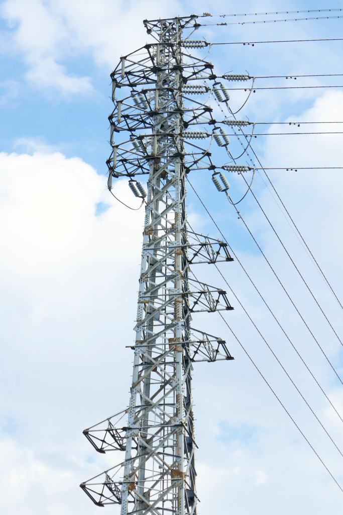 高圧送電線の鉄塔の写真。 雲のある空を背景に鉄骨の塔が立つ。 送電線が幾本も伸びている。
