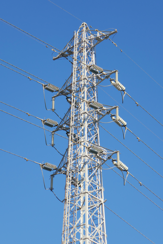 高圧送電線の鉄塔の写真。 青空を背景に鉄骨の塔が立つ。 送電線が幾本も伸びている。