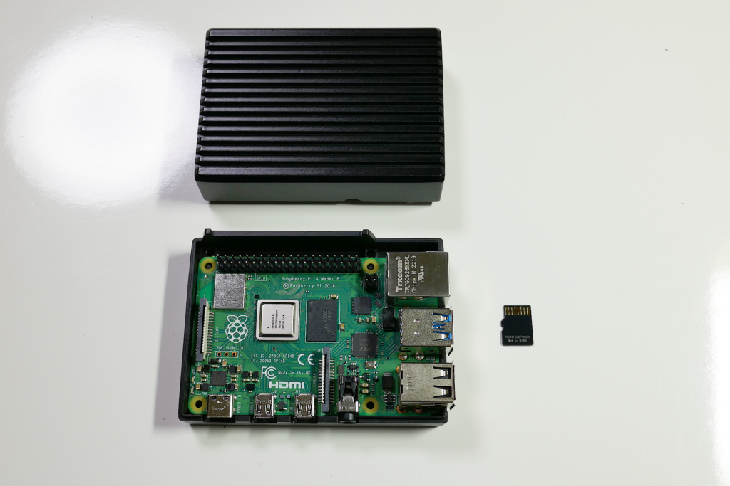 黒色のアルミニウム製のケースに収められたRaspberry Pi 4 Model BとmicroSDメモリー カードを正面上方から撮影した写真。 ケースの上蓋が外されて上方に置かれて基板が見えている。 右隣りにmicroSDメモリー カードが置かれている。