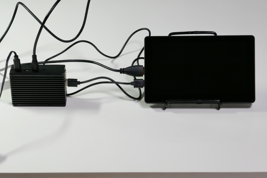 黒色のアルミニウム製ケースに収められたRaspberry Pi 4 Model Bと小型ディスプレイを撮影した写真。 画面は電源が切られて黒い。 Raspberry Pi 4 Model B本体とディスプレイにはケーブル類が幾本も繋がっている。