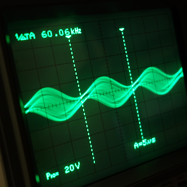 オシロスコープの画面の写真。 正弦波のノイズ波形が映し出されている。 周波数は凡そ60kHzとなっている。