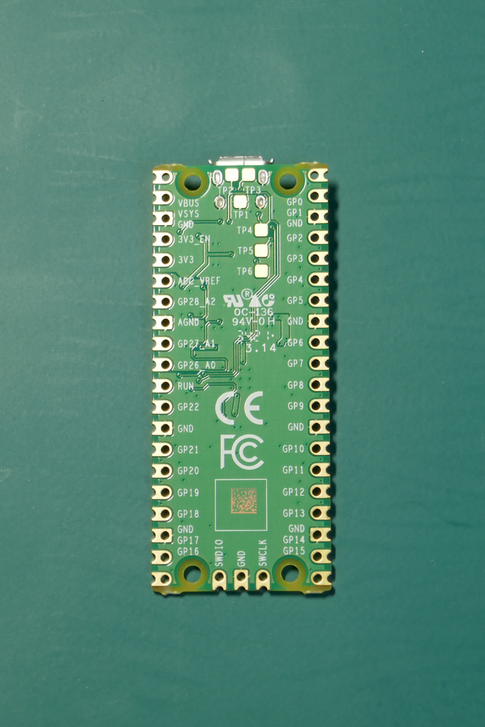 Raspberry Pi Picoの基板が緑色のゴム マットの上に縦向きに裏返しで置かれている写真。