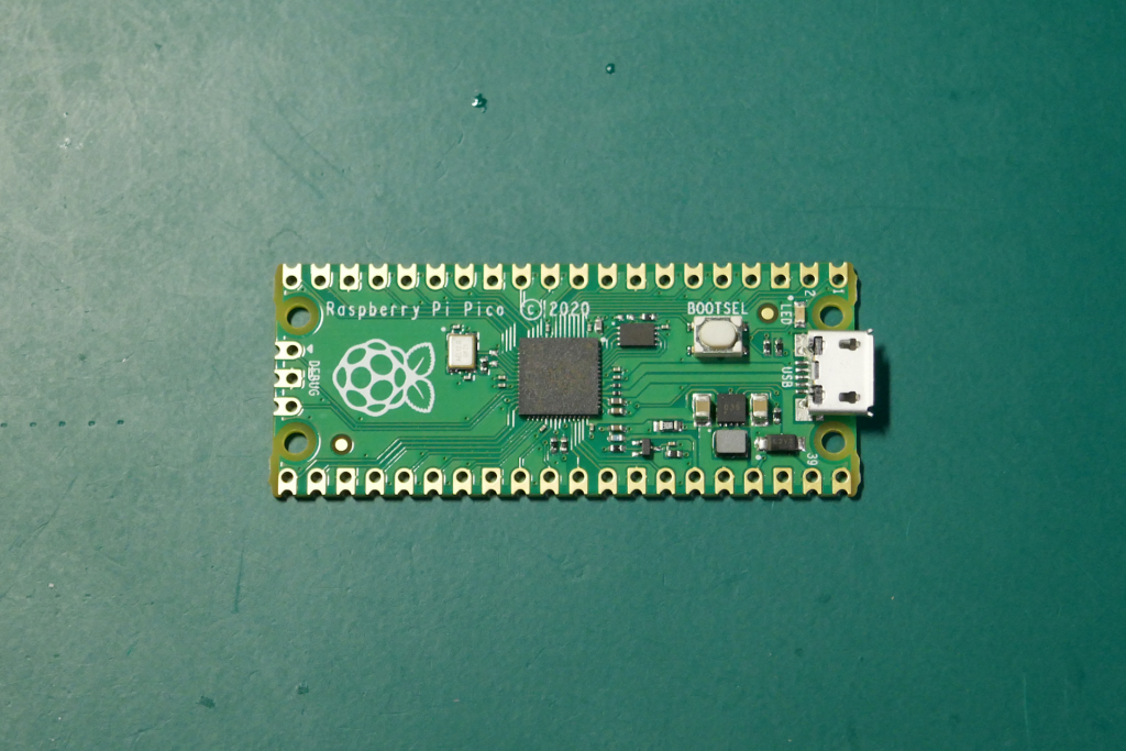 Raspberry Pi Picoの基板が緑色のゴム マットの上に横向きに置かれている写真。